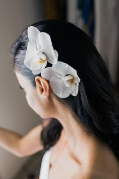 a woman with long black hair and white flowers in her hair is looking at the mirror