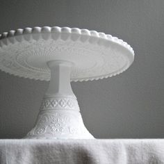 a white cake plate sitting on top of a table next to a towel and wall