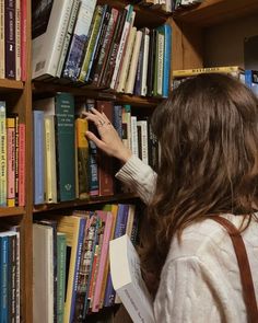 a woman is reaching for books on a book shelf in a library with many books