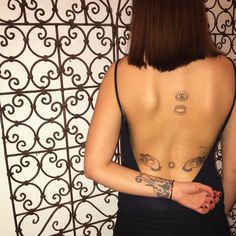 a woman with tattoos on her back standing in front of a wall and iron gate