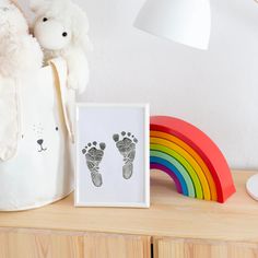 a white teddy bear sitting next to a baby's foot print and a rainbow