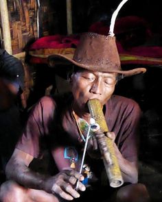 a man wearing a brown hat and holding a pipe in his hand while sitting down