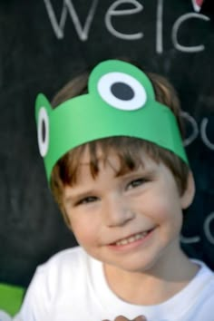 a young boy wearing a green hat and holding a donut in front of a chalk board