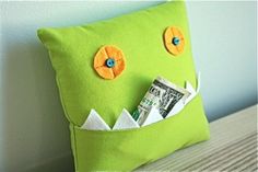 a green monster pillow with money sticking out of it's mouth, sitting on a bed