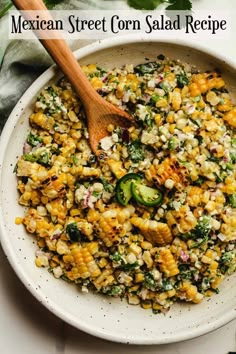 a bowl filled with corn and vegetables on top of a white table next to a wooden spoon