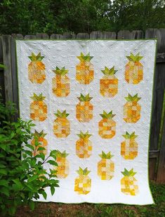 a quilt made with pineapples is hanging on a fence in front of some bushes