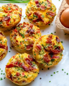 several breakfast muffins with bacon and chives on a white plate next to an egg