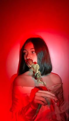 a woman in a red dress holding a rose up to her face and looking at the camera