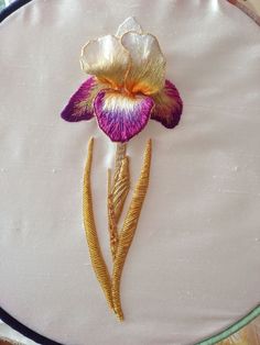 a close up of a flower on a white cloth with gold thread and sequins