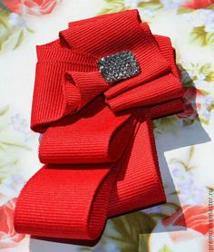 a red bow with a diamond brooch sits on a flowered tablecloth,