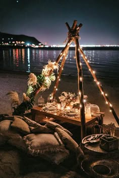 a table is set up on the beach with lights strung from it and candles in front