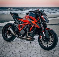 an orange and black motorcycle parked on the beach