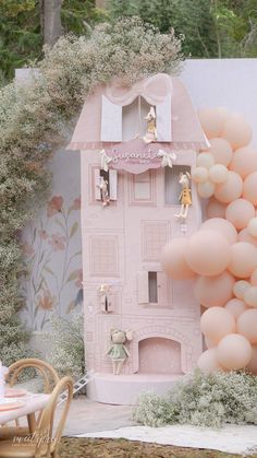 a pink doll house with balloons in the shape of people on top and around it