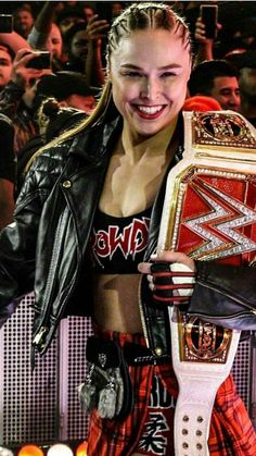 a woman holding a wrestling belt in front of a crowd