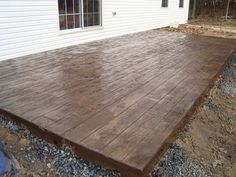 a wooden deck in front of a white house with gravel on the ground next to it