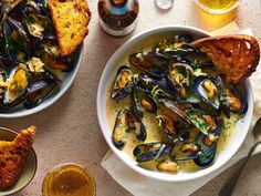 two bowls filled with mussels and bread on top of a table next to drinks