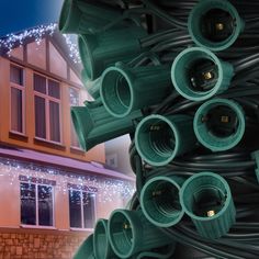 many green pipes are stacked on top of each other in front of a house with christmas lights