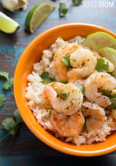 a bowl filled with rice and shrimp on top of a wooden table next to lime wedges