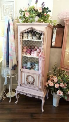 an old china cabinet with flowers and other items on it's shelves next to a potted plant