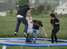 four young people jumping on a trampoline in the rain with their arms outstretched