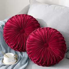 two red pillows sitting on top of a bed next to a cup and saucer