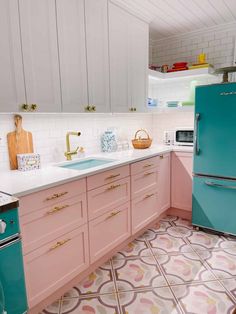 a kitchen with pink and blue cabinets, white counter tops, and patterned floor tiles