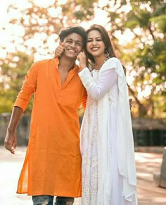 two people standing next to each other in an orange and white outfit with trees in the background