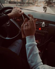 two hands on the steering wheel of a car as it drives down a city street