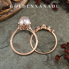 two gold rings with pearls on them sitting next to some rocks and flowers in the background