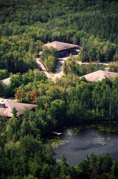 an aerial view of a house surrounded by trees and water in the foreground is a wooded area