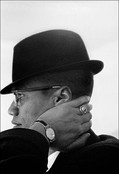 a man wearing a hat and glasses is holding his hand to his face while looking off into the distance