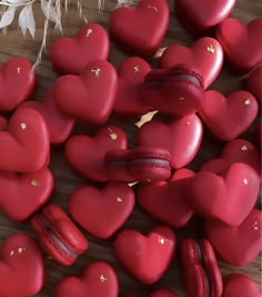 heart shaped red macaroons with gold flecks on a wooden table next to feathers