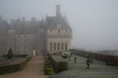 an old castle in the fog with lots of hedges and bushes on either side of it