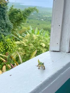 a small toy lizard sitting on top of a window sill next to a lush green forest