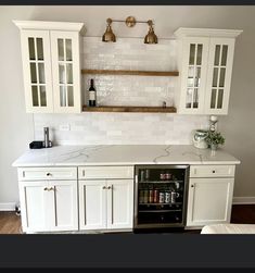 a kitchen with white cabinets and marble counter tops, an open wine cooler in the center