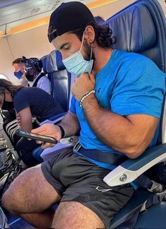 a man sitting in an airplane wearing a face mask and looking at his cell phone