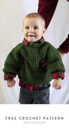 a baby wearing a green sweater and smiling at the camera with his hands on his hips