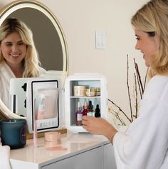 a woman is looking at her reflection in the mirror as she opens an open refrigerator