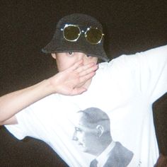 a man wearing sunglasses and a hat covering his face with his hands while standing in the dark