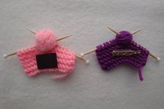 two knitted pins are sitting next to each other on a white surface with pink and purple yarn