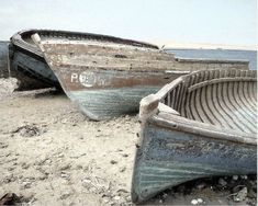 two boats sitting on top of a sandy beach next to the ocean with no people