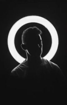 a man standing in front of a circular light with his head turned to the side