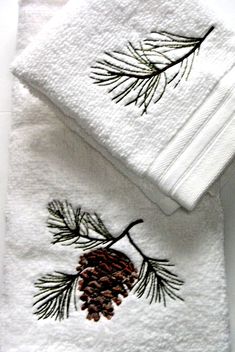 two white towels with pinecones on them and one is embroidered onto the towel