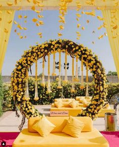 an outdoor ceremony area with yellow flowers and hanging decorations on the ceiling, along with white linen covered tables