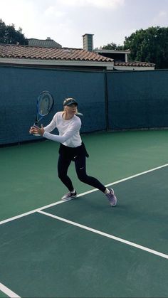 a woman holding a tennis racquet on top of a tennis court with buildings in the background