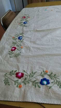 an embroidered table cloth with flowers and leaves on it, sitting on a dining room table