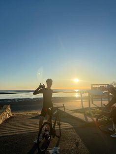 a person on a bike with the sun setting in the back ground and water behind them