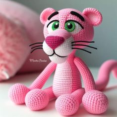 a crocheted pink cat sitting on top of a white table next to a pillow