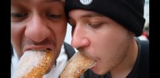 two men with hats and beanies are eating donuts in front of each other