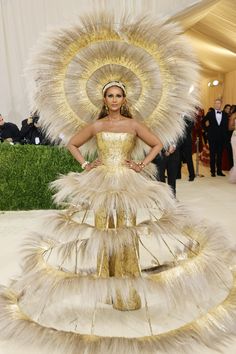 a woman in a gold and white dress with feathers on her head, posing for the camera